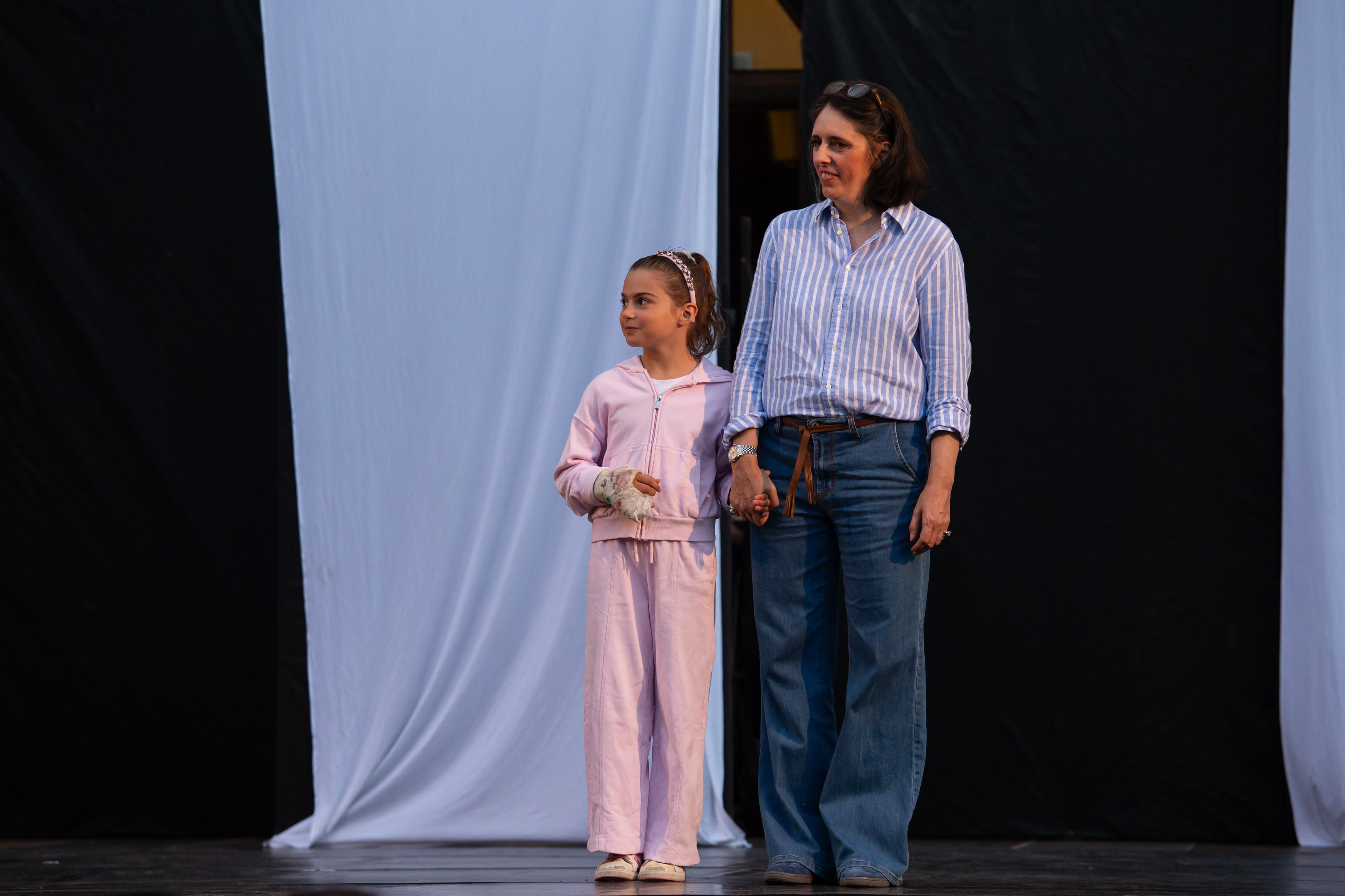 Donna e bambina in tuta rosa con mano bendata si tengono per mano sul palco.