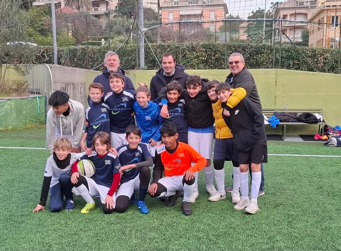 Squadra di calcio giovanile e allenatori sorridenti in posa per una foto sul campo.