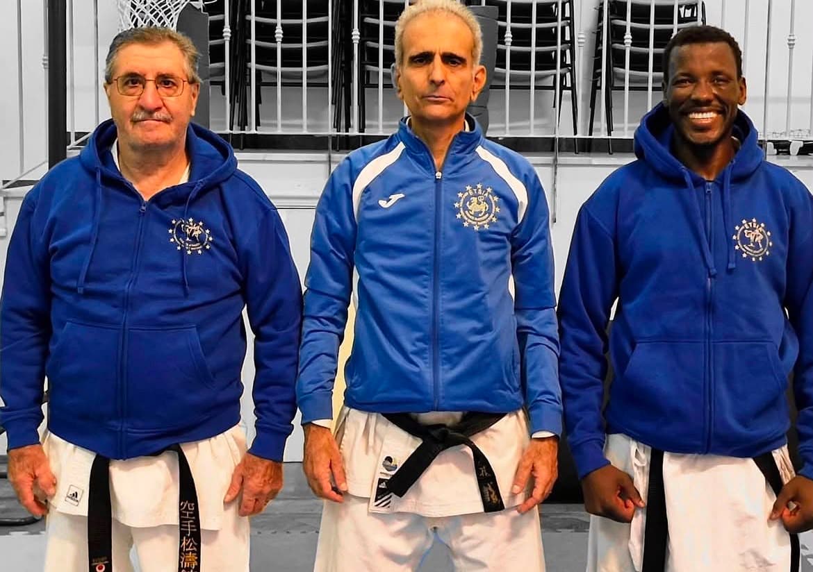 Tre uomini con cinture nere di karate indossano giacche blu sopra le divise bianche.