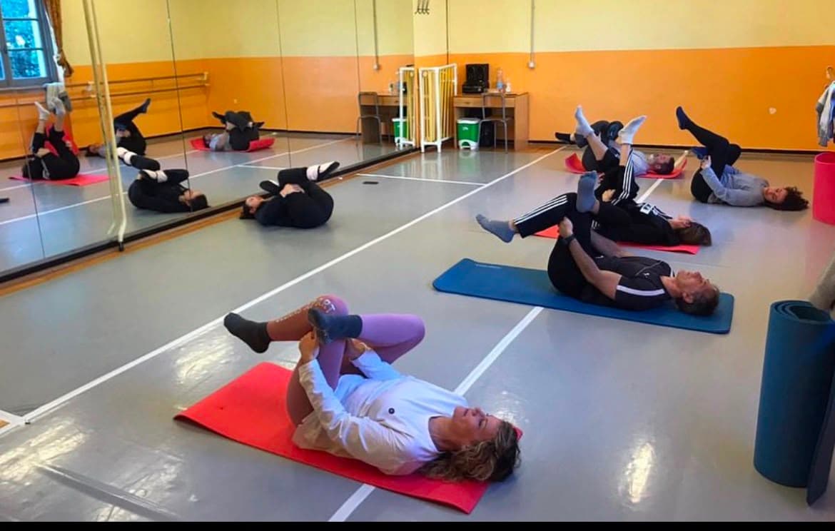 Persone in una palestra che eseguono esercizi di stretching a terra su tappetini colorati.