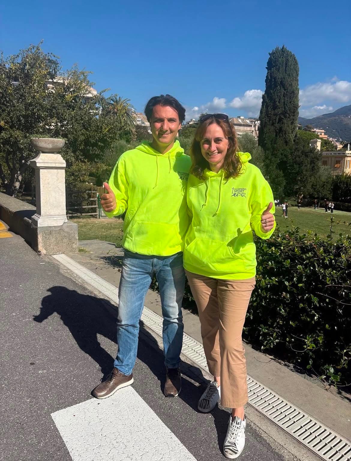 Uomo e donna in felpe giallo neon sorridono facendo il pollice in su all'aperto.