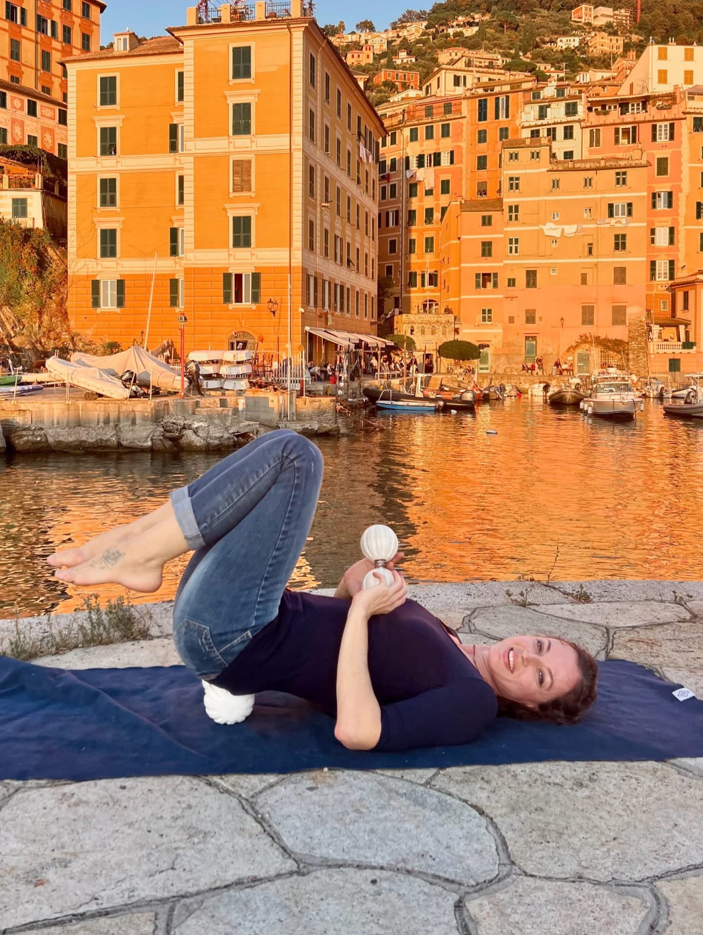Donna sdraiata su un tappetino usa palline massaggianti nel porto di Camogli al tramonto.